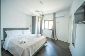 Habitació d'hotel amb un llit gran, una taula de nit, una finestra amb cortines i un aire acondicionador integrat.