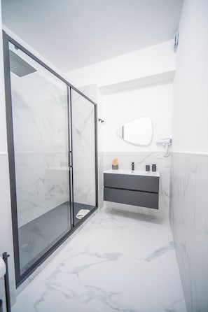 A modern bathroom with a glass shower enclosure, a vanity with a mirror, and marble-patterned walls.