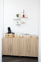 Un mueble de madera con cajones, un pequeño estante con plantas y un espejo redondo en la pared.