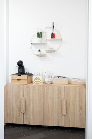 A wooden cabinet with drawers, a small shelf with plants, and a round mirror on the wall.