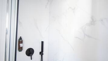 A shower with a black rain showerhead, a handheld showerhead, and a bottle of shampoo on the wall.