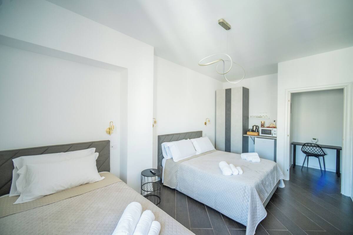 A hotel room with two beds, a desk, a chair, and a small kitchenette.