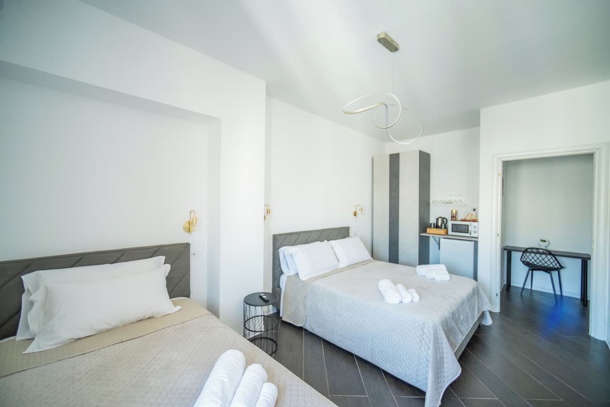 A hotel room with two beds, a desk, a chair, and a small kitchenette.