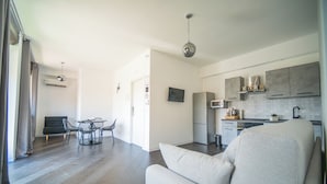 A modern living room with a sofa, a dining table with chairs, a kitchen area with cabinets and appliances, and a TV mounted on the wall. - Newhouse ARGIRO Deluxe (Bari)