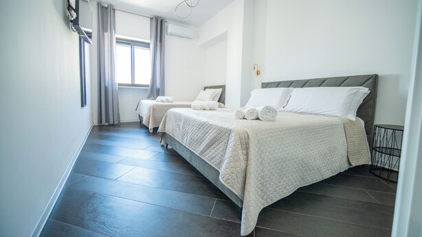 A hotel room with two beds, a large window with curtains, a flat-screen TV mounted on the wall, and a small table by the window. - Newhouse ARGIRO Deluxe (Bari)