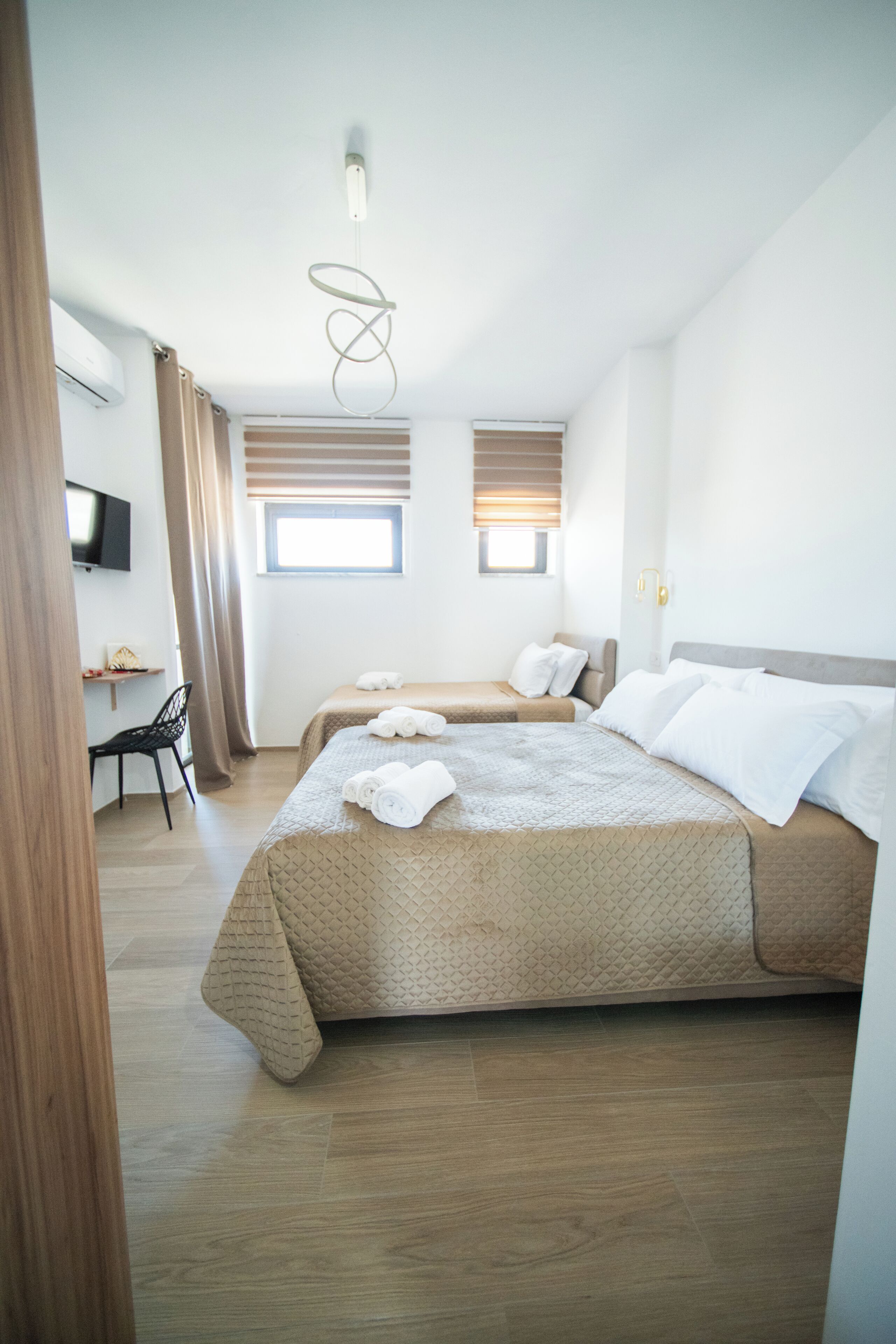 A hotel room with two beds, a desk, a chair, a TV, and a window with curtains.