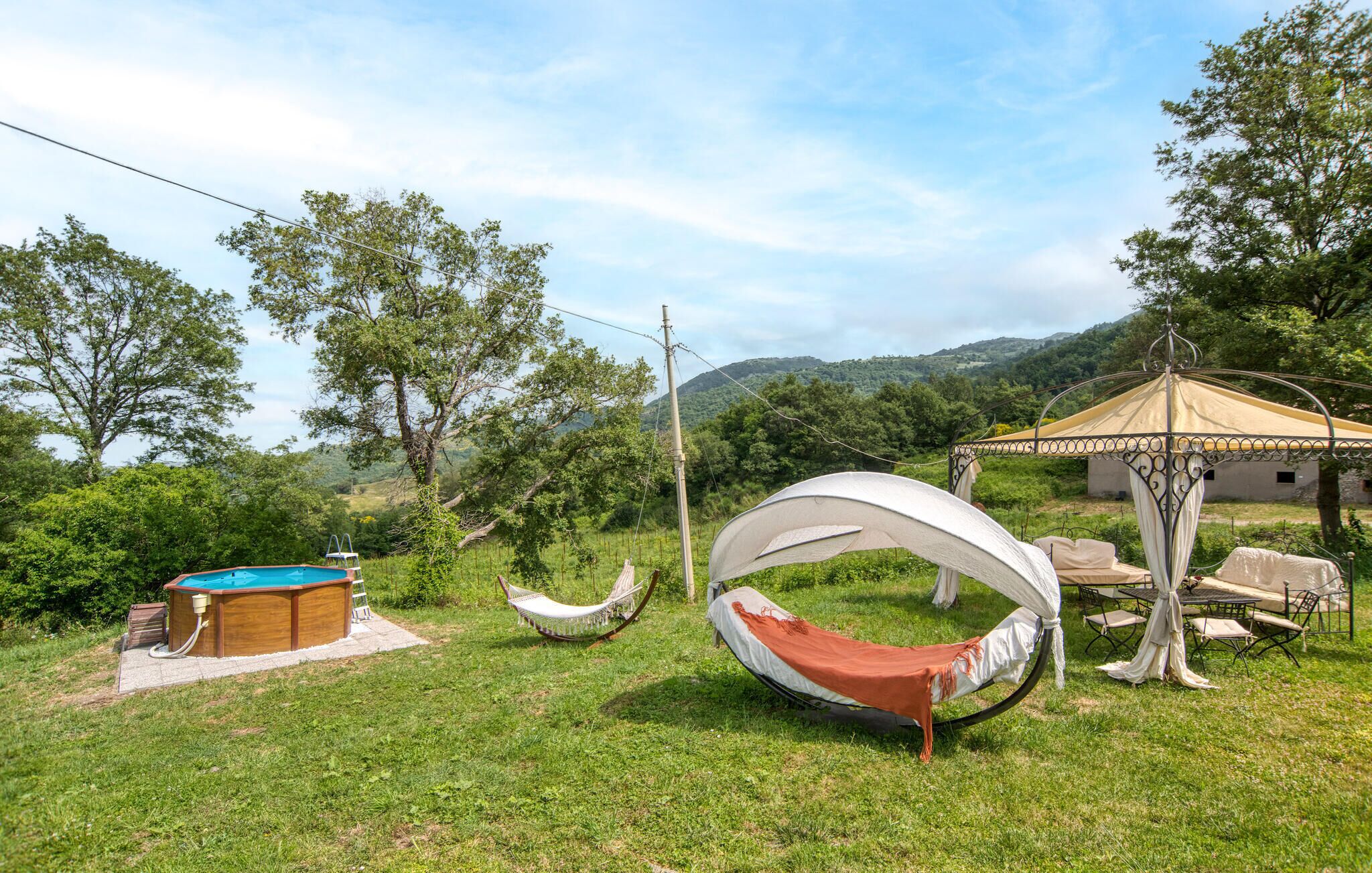 A hammock, a small pool, and a gazebo in a grassy area with trees and hills in the background.