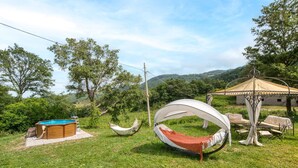 Eine Hängematte, ein kleiner Pool und ein Pavillon in einer grünen Umgebung mit Bäumen und Hügeln im Hintergrund.