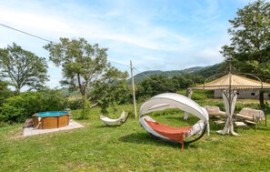 Uma rede, uma piscina pequena e um gazebo em área gramada, com árvores e colinas ao fundo.