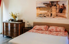 Ein Schlafzimmer mit einem Bett, einem Schminktisch, einem Nachttisch, einer Vase mit Blumen und einem Bild an der Wand.