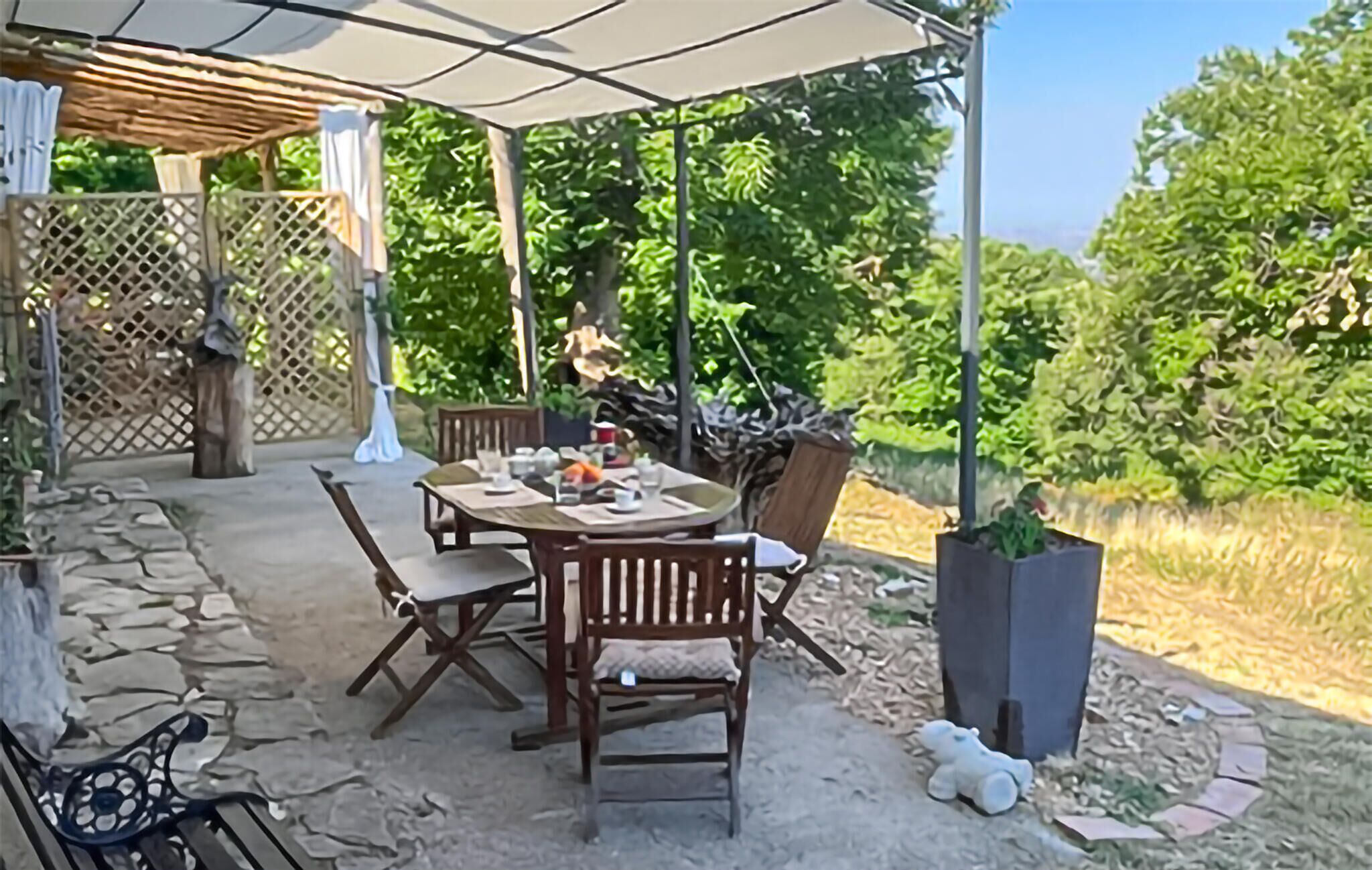 Um pátio externo com mesa e cadeiras, cercado por um portão de madeira e vegetação.