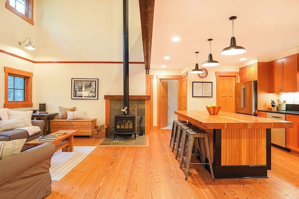 A spacious living room with a fireplace, wooden flooring, and a kitchen with wooden cabinets and a bar area.
