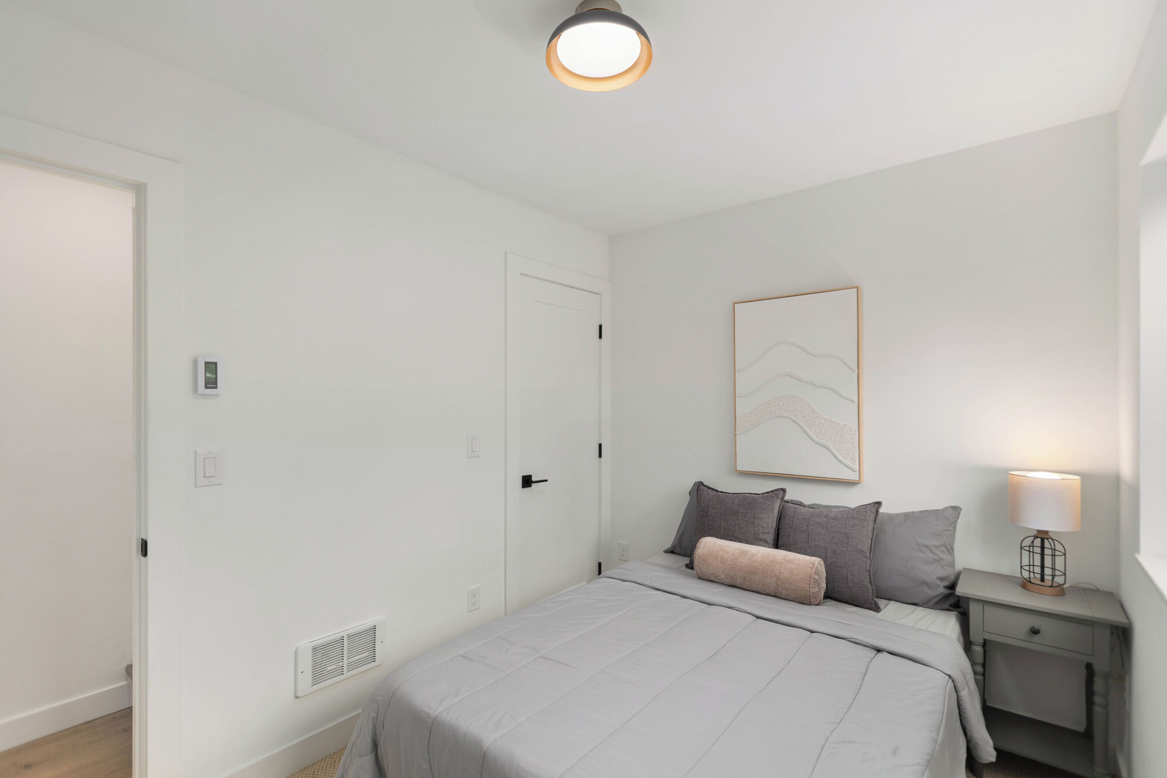 Een slaapkamer met een bed, nachtkastje, lamp en een deur.