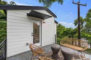 Ein kleines Gebäude mit einer Tür, zwei Korbstühlen und einem Tisch auf einer Terrasse.