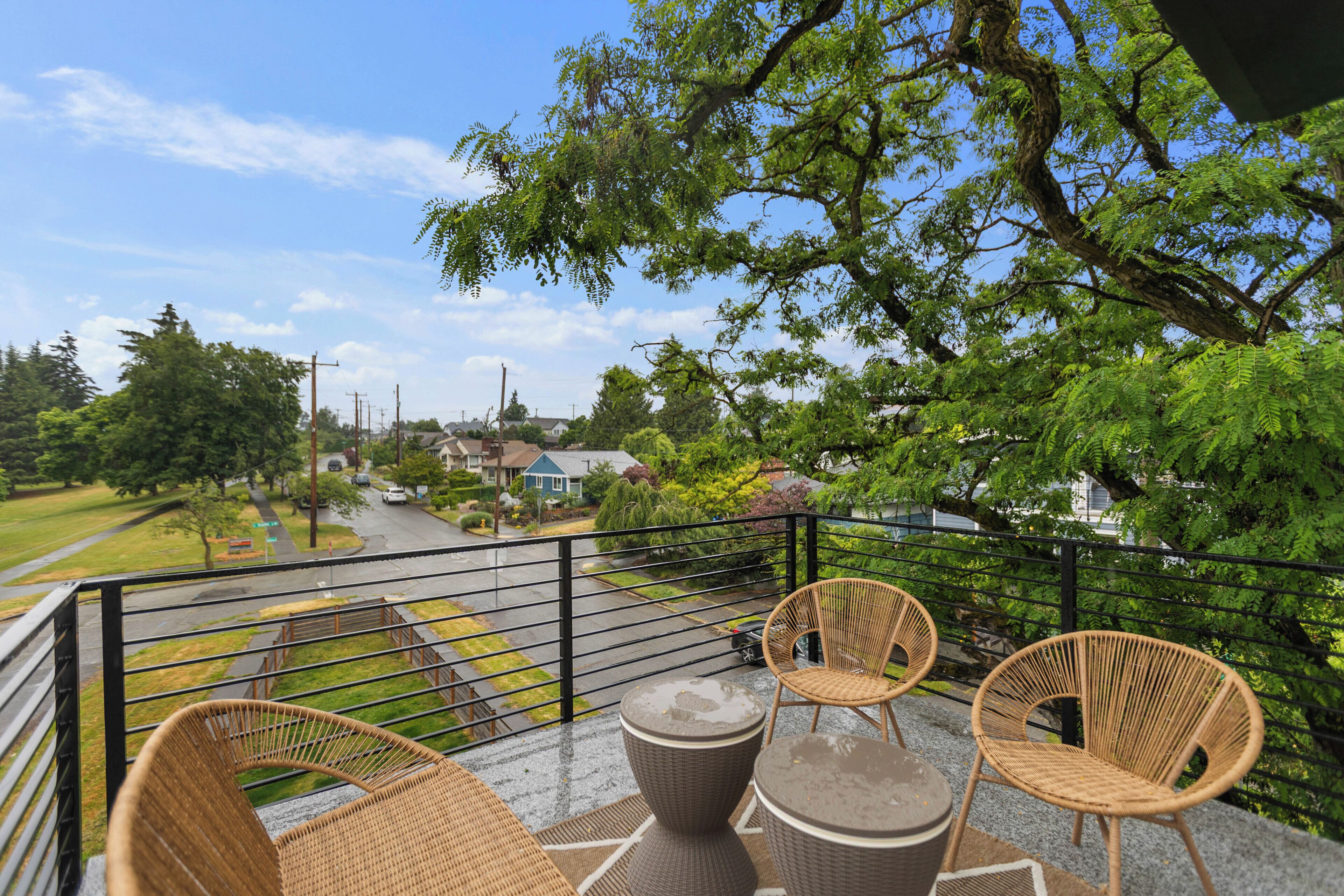 A balcony with wicker furniture, a view of a street, and a tree.