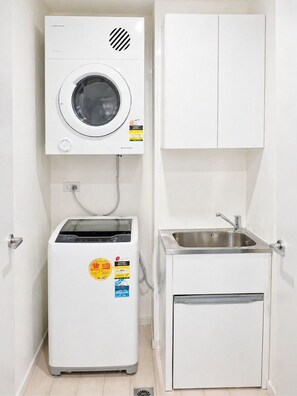 A compact utility room with a washing machine, a small refrigerator, and a sink. - Modern Studio in Zetland | Close to CBD, Airport & Green Square (Zetland)