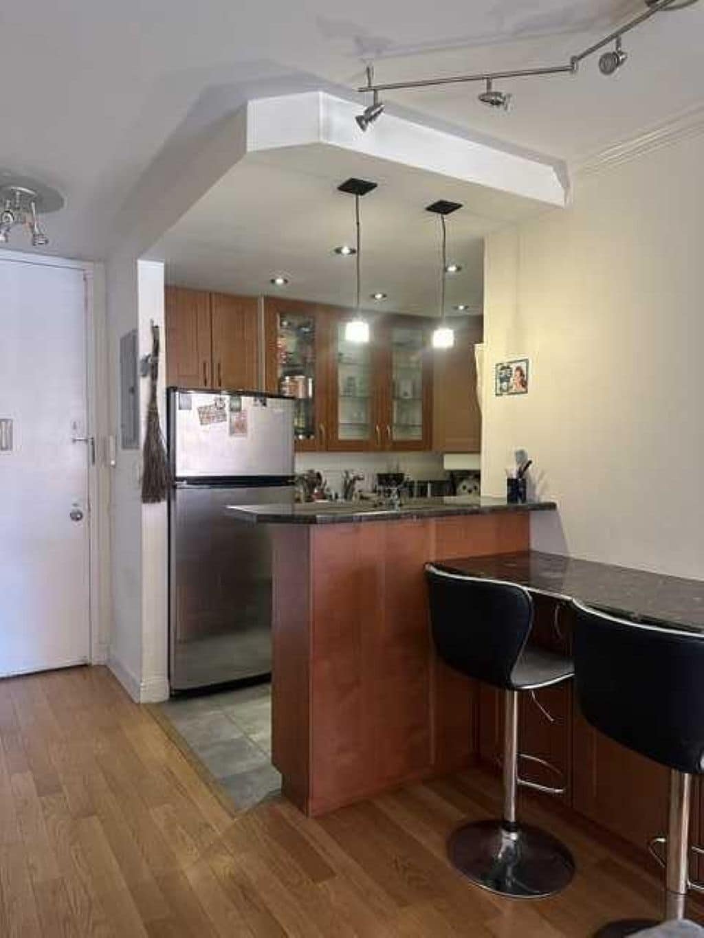 Eine moderne Küche mit Holzausstattung, einem Edelstahlkühlschrank und einer Bar mit zwei Hockern.