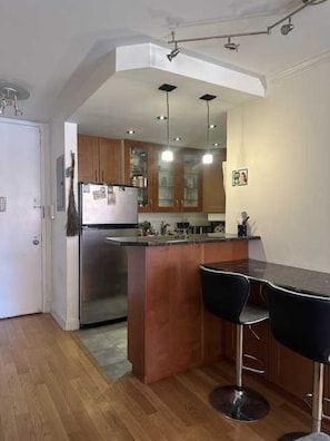 Eine moderne Küche mit Holzausstattung, einem Edelstahlkühlschrank und einer Bar mit zwei Hockern.