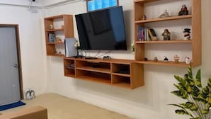 Ett vardagsrum med en väggmonterad TV, trähyllor och en krukväxt.