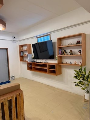 Un salon avec un téléviseur fixé au mur, des étagÚres en bois et une plante en pot.