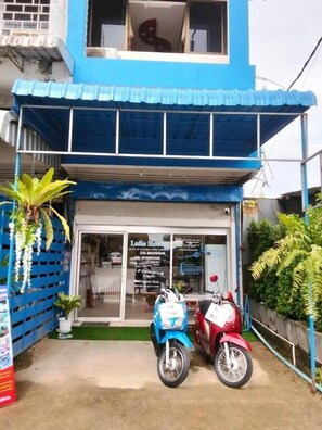 A two-story building with a blue facade, a visible entrance, and two parked scooters.