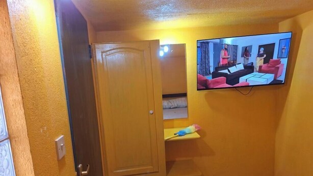 Una stanza con televisione a parete, una porta e un piccolo ripiano con un giocattolo.