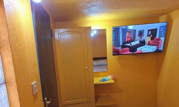 A room with a television mounted on the wall, a door, and a small shelf with a toy. - Welcoming apartment with AC in the heart of Oxnards (Oxnards)