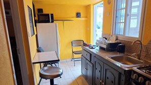 Una cucina compatta con frigorifero, microonde, lavello e un piccolo angolo ristoro con una sedia e un tavolo.