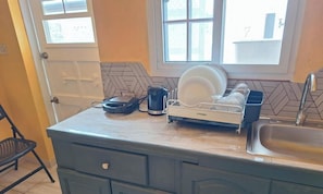 A kitchen with a dish rack, a kettle, and a coffee maker on the counter. - Welcoming apartment with AC in the heart of Oxnards (Oxnards)