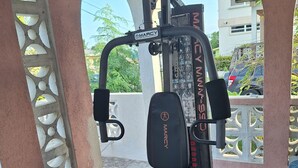 Una palestra con un attrezzo Marcy, pavimento piastrellato e vista su una zona residenziale attraverso una finestra ad arco.