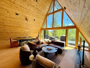 A high-ceilinged wooden interior with a dining area, seating, and large windows.