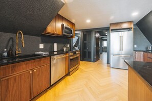 A modern kitchen with wooden cabinets, stainless steel appliances, and a herringbone floor pattern. - Lakeview A-Frame with hot tub near RMNP (Grand Lake)