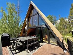 A modern A-frame building with a deck, outdoor seating, and large windows.