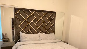 Une chambre moderne avec une tête de lit aux motifs géométriques, un grand miroir et un plancher en bois.
