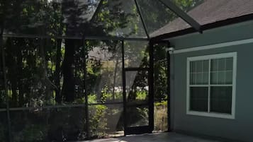 Une piscine dotée d’une enceinte en verre, des marches menant à l’eau et une maison en arrière-plan.