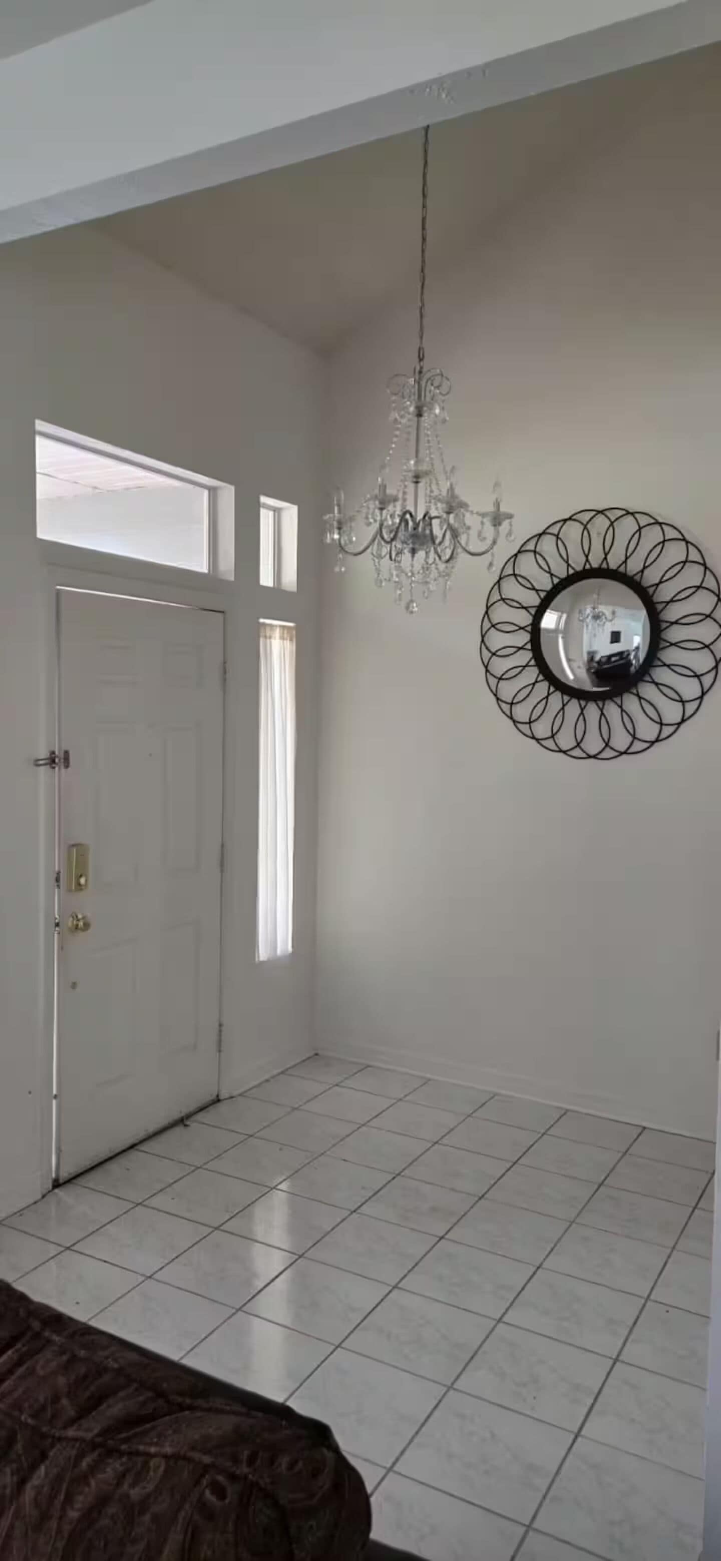 Une pièce avec un lustre, un miroir rond, une porte blanche et une fenêtre.