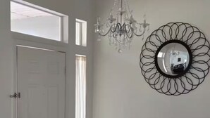 A room with a chandelier, a round mirror, a white door, and a window.