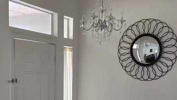 Une pièce avec un lustre, un miroir rond, une porte blanche et une fenêtre.