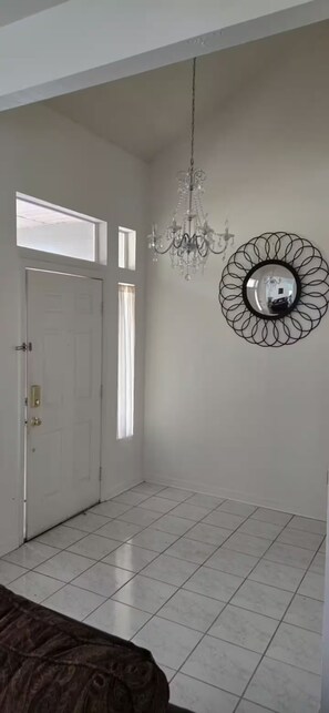 Une pièce avec un lustre, un miroir rond, une porte blanche et une fenêtre.