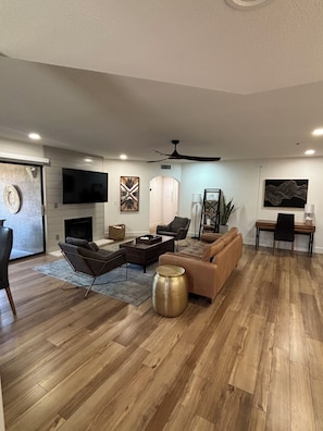 A modern living room with a fireplace, a flat-screen TV, and a ceiling fan.