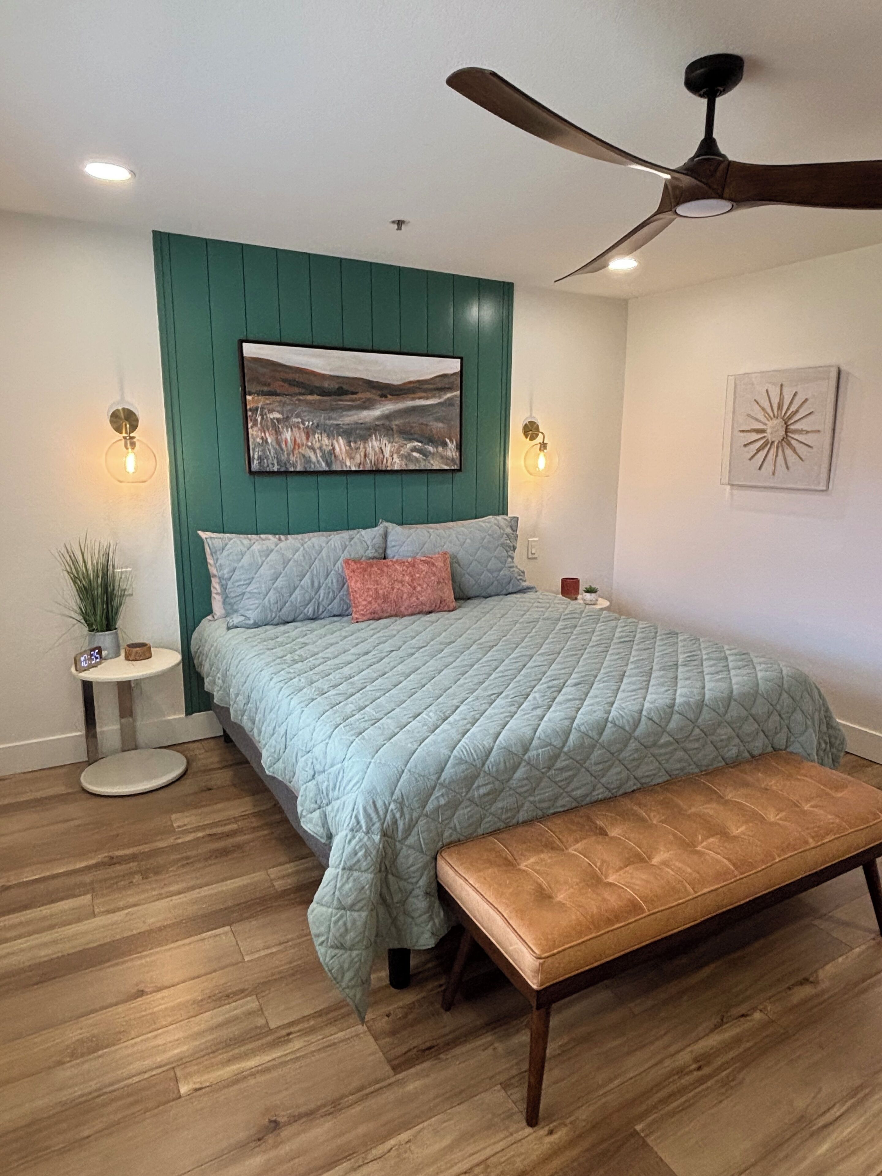 A bedroom with a bed, a ceiling fan, a wall-mounted painting, and two bedside lamps.