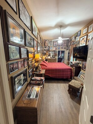 Ein Schlafzimmer mit Bett, Schreibtisch, Stuhl, Fernseher und an den Wänden angebrachten gerahmten Bildern.
