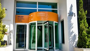 Entree van een bedrijfspand met een draaideur van glas, borden met 'COMERCIO Sudeste Fluminense RJ' erop en het nummer '201' op de muur.