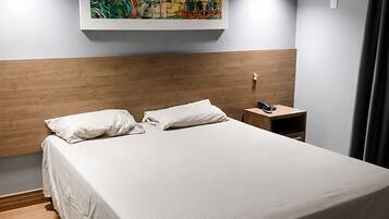 Une chambre d’hôtel moderne avec un grand lit, une tête de lit en bois, une table de chevet, un appareil de climatisation et un tableau au mur.