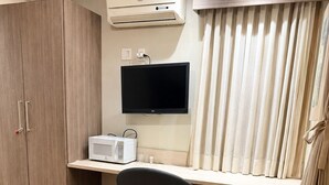 Een hotelkamer met een houten garderobe, een bureau met een flatscreen televisie, een magnetron, een stoel, een kleine koelkast en een bed met een oranje sprei.