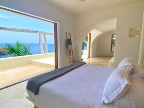Une chambre avec un grand lit, une vue sur l’océan et un balcon.