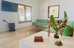 Un salon avec un canapé vert, une table blanche ornée de blocs de bois, une plante et une fenêtre donnant sur un paysage verdoyant.