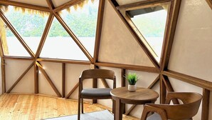 Una estructura tipo tienda con piso de madera, dos sillas, una mesita y una planta en maceta.