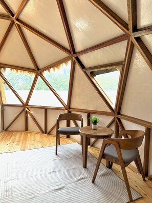 Eine zeltähnliche Konstruktion mit Holzboden, zwei Stühlen, einem kleinen Tisch und einem Blumentopf.