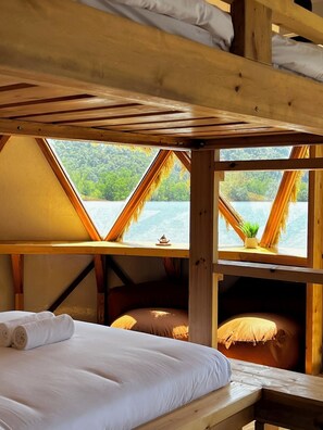 A wooden cabin with a bed, a bench, and a view of a lake through triangular windows. - Coconest TWO: Floating Geodesic Dome Waterstay on a UNESCO Site (Langkawi)